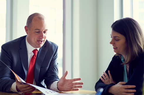 A man and woman look at a brochure and talk.