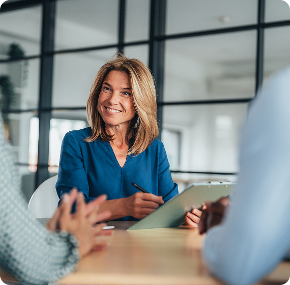 Image of financial advisor smiling while meeting with clients and taking notes at a table.
