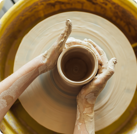 Image of hands shaping a clay pot on a pottery wheel.