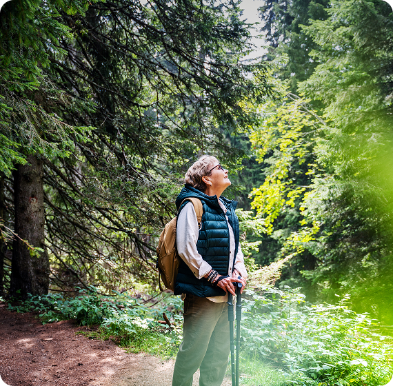  Image of woman hiking in a forest, pausing to look up at the trees.