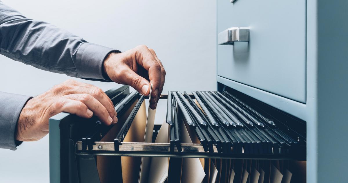 Two hands sifting through a filing cabinet.