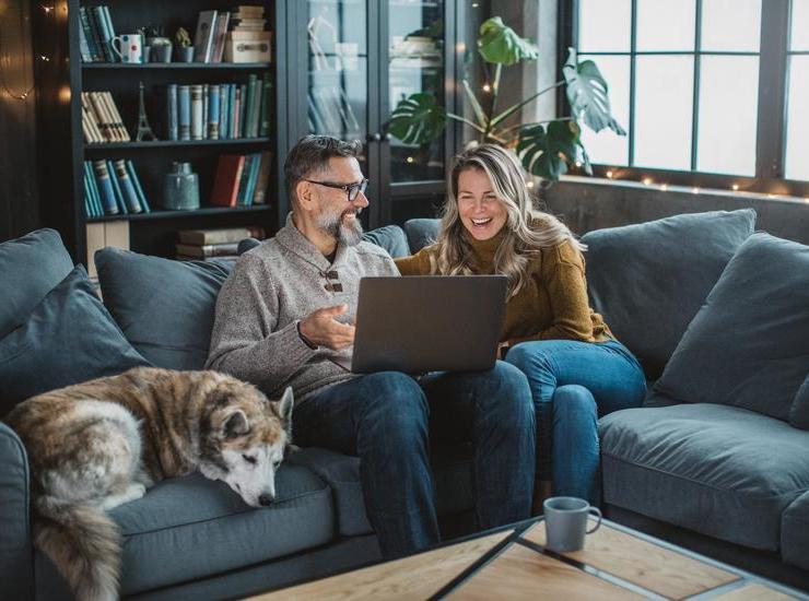 Family with a dog sitting on couch using a laptop.