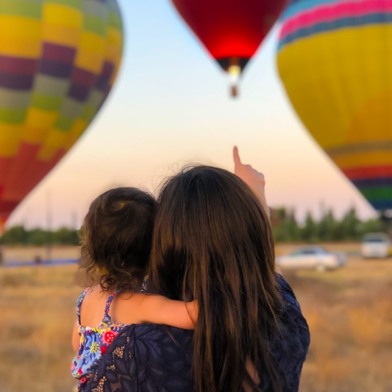 A mother holding her child and pointing to hot air balloons.